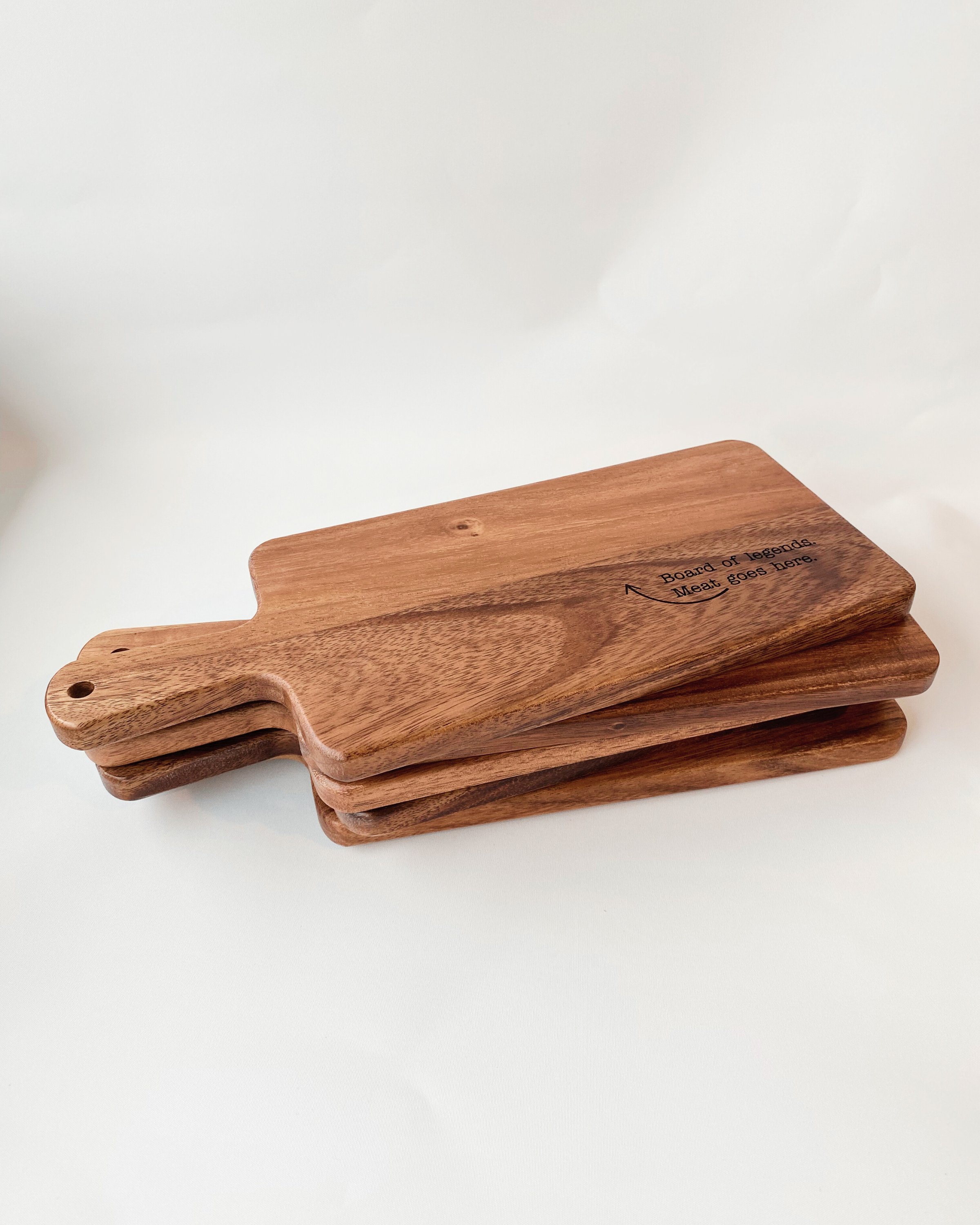 A stack of Dad Board chopping or serving board engraved with 'Board of Legends. Meat Goes Here." Made from food-grade acacia wood.