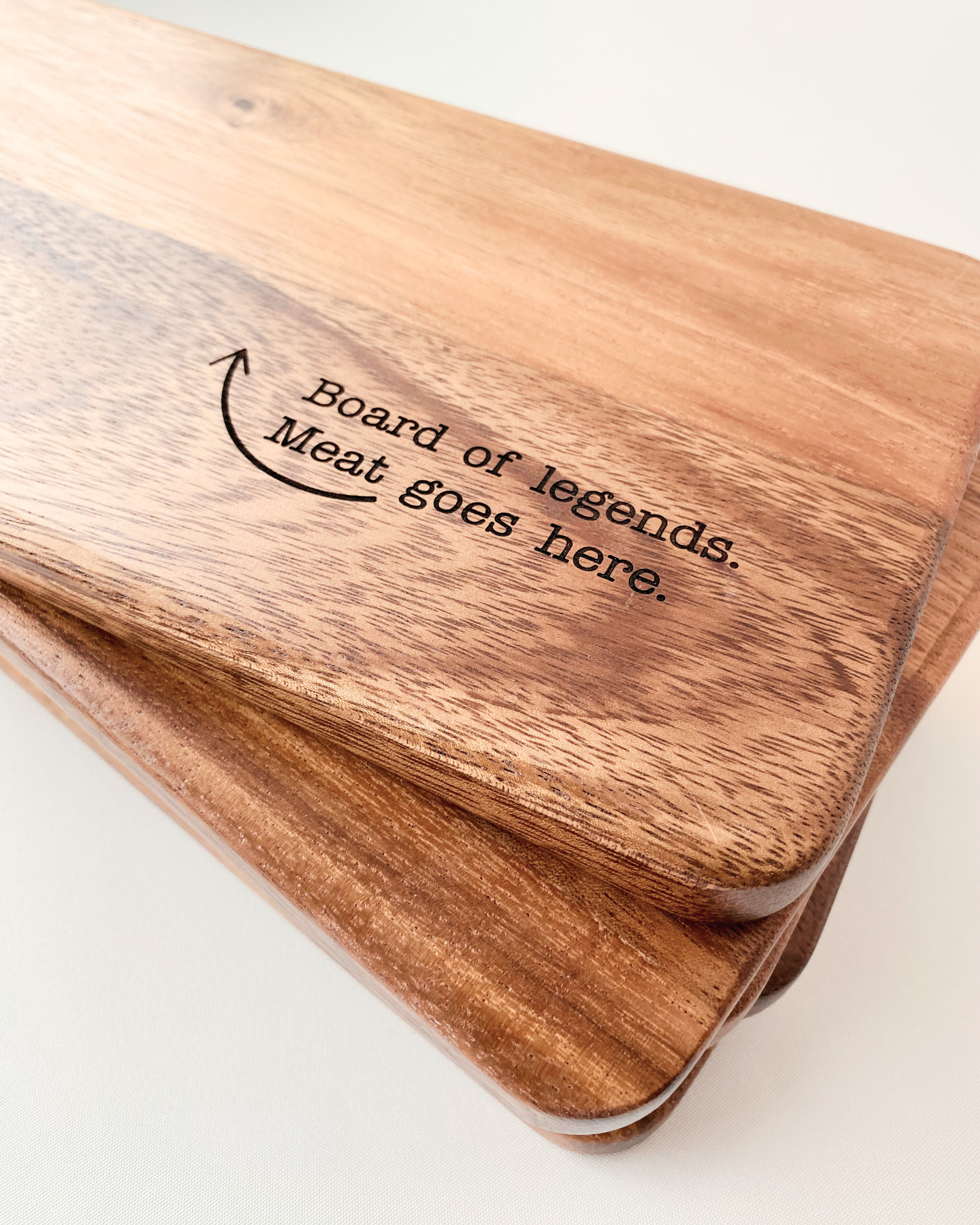 A stack of Dad Board chopping or serving board engraved with 'Board of Legends. Meat Goes Here." Made from food-grade acacia wood.