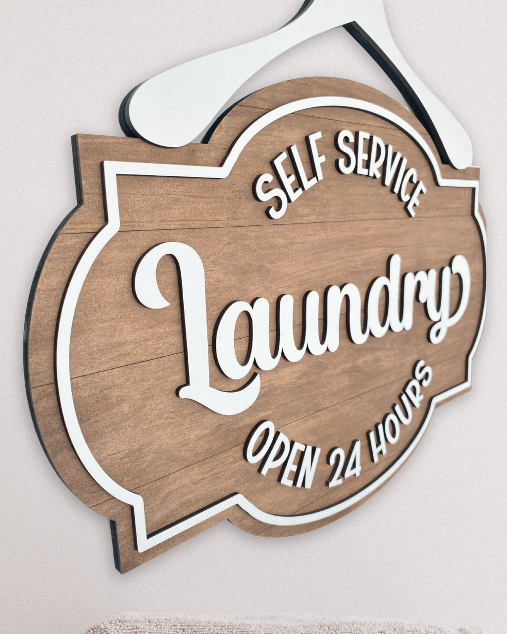 Wooden sign with 'Self Service Laundry Open 24 Hours' text on a light background