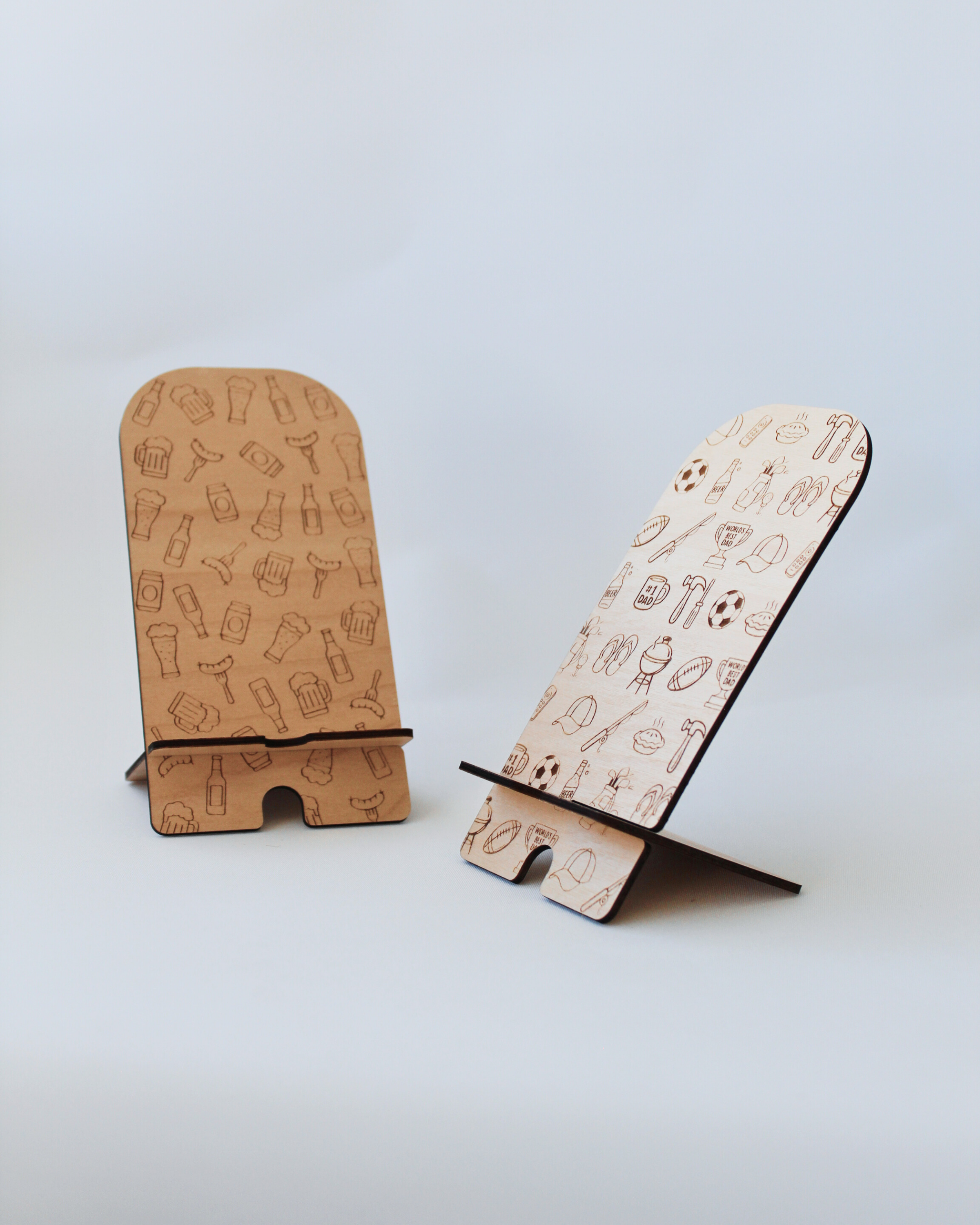 Wooden Phone Stands in the Beer & Sausages and Classic Kiwi Dad designs against a white background.