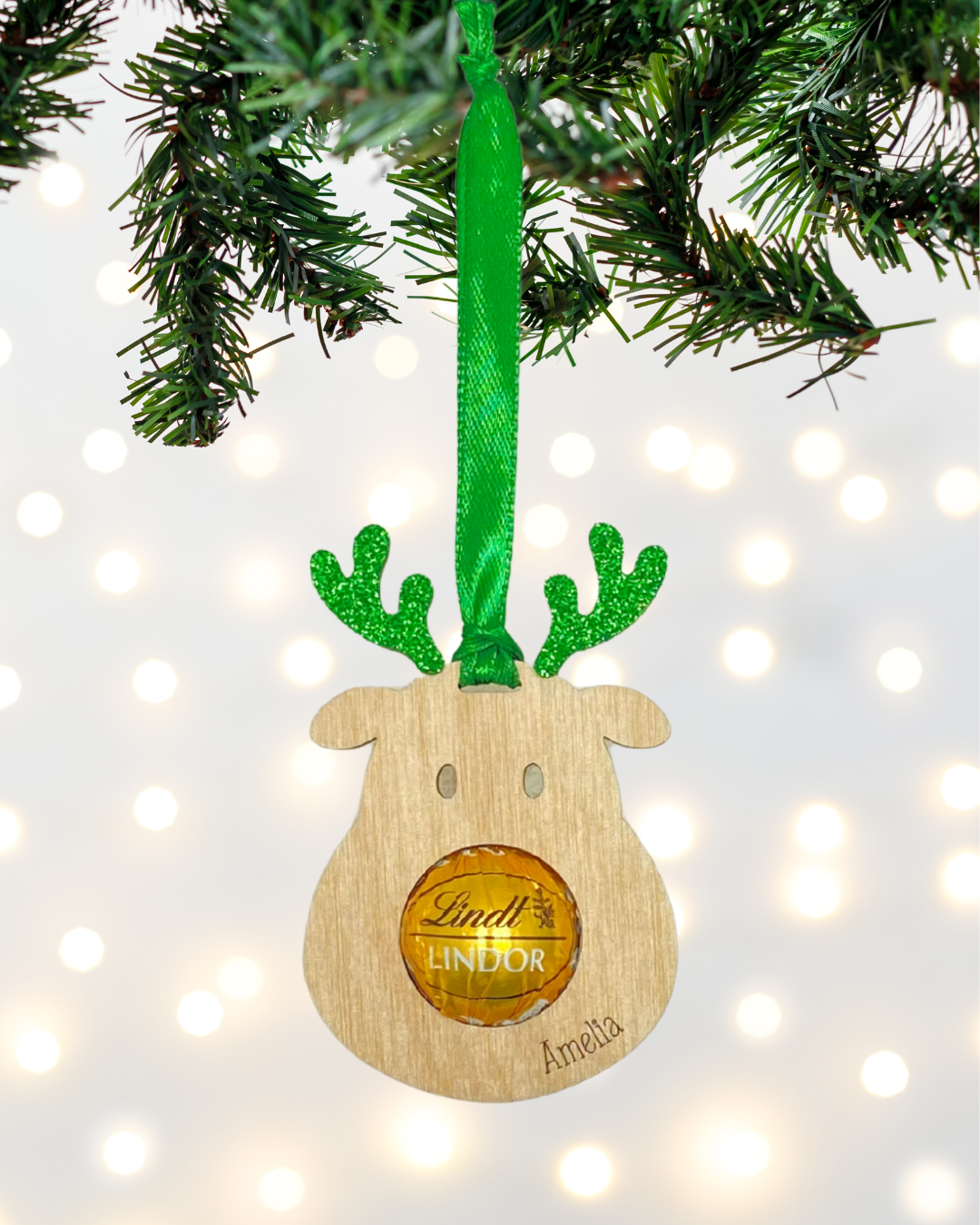 Laser-cut wooden Sweet-Nose Reindeer Ornament in green with a Lindt chocolate nose, engraved with the word Amelia.