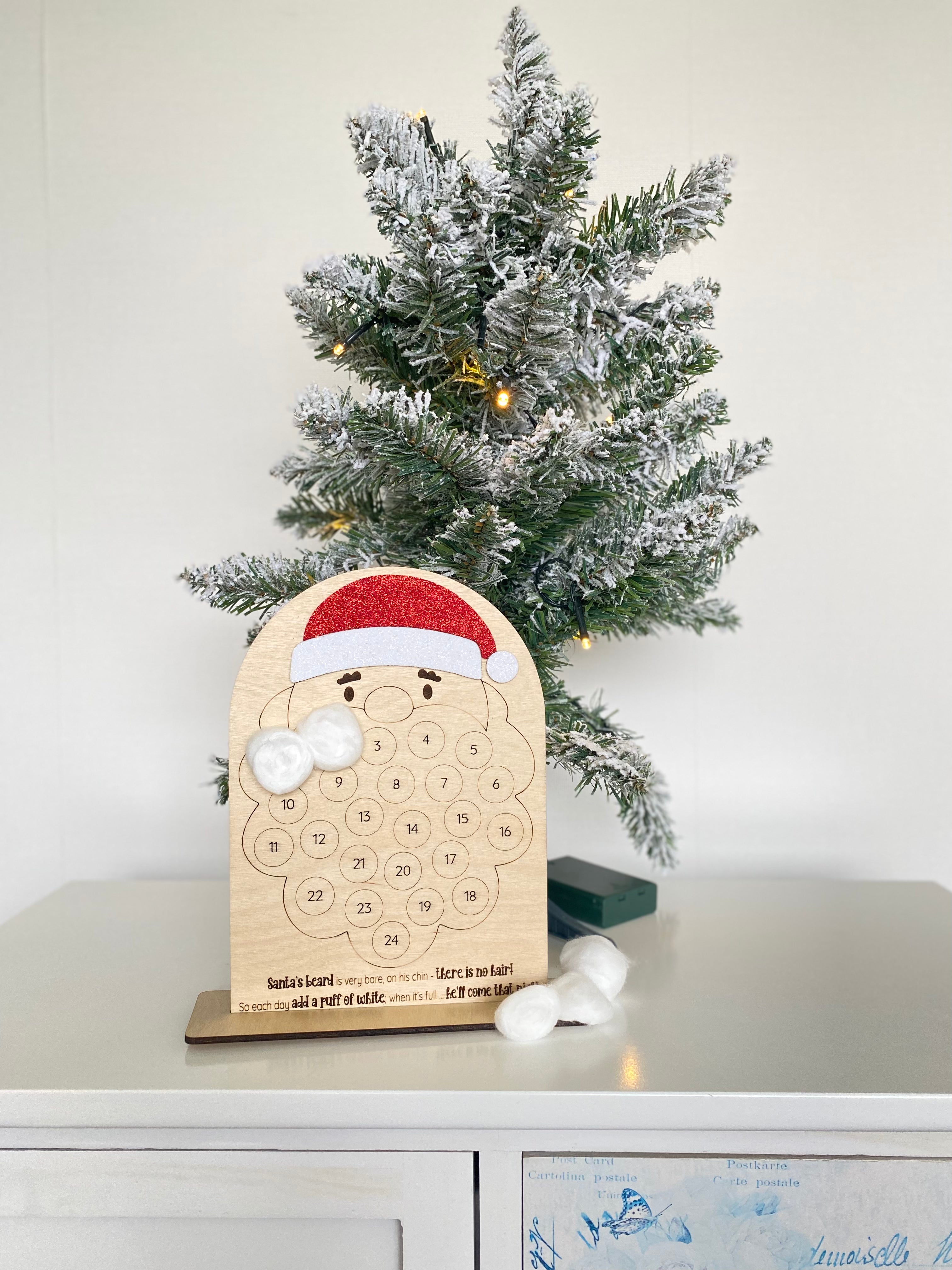 Wooden advent calendar placed next to a mini Christmas tree, in the shape of Santa Claus. Place cotton balls onto the sticky dots and fill out his beard each day of the advent.