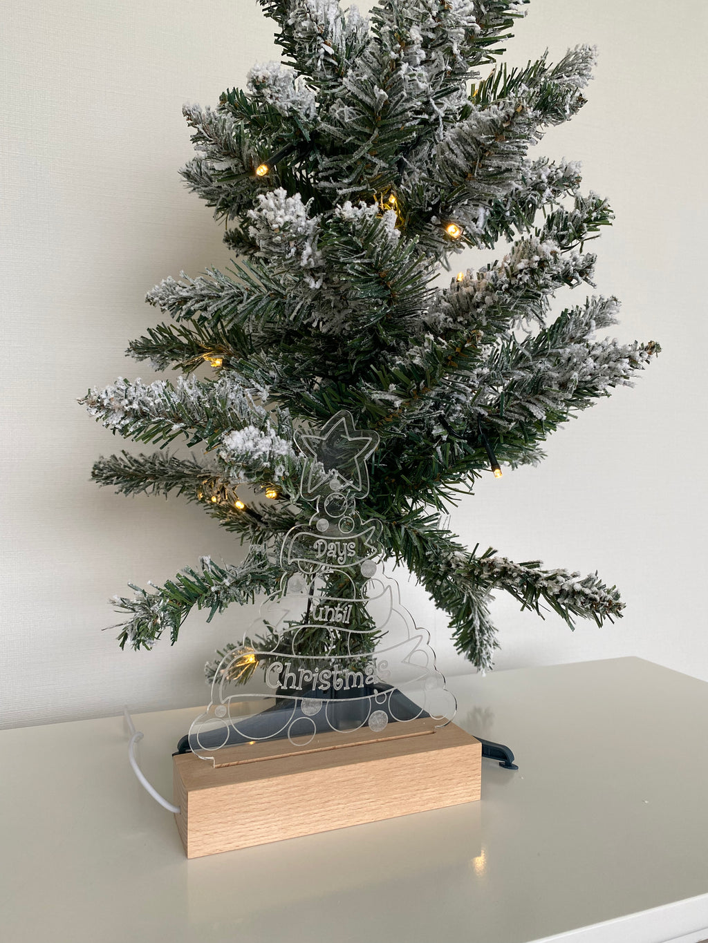 Christmas Countdown Night Light placed next to a mini Xmas tree, made from clear acrylic on a wooden base, complete with a whiteboard marker to write down each day of advent. Powered by USB.