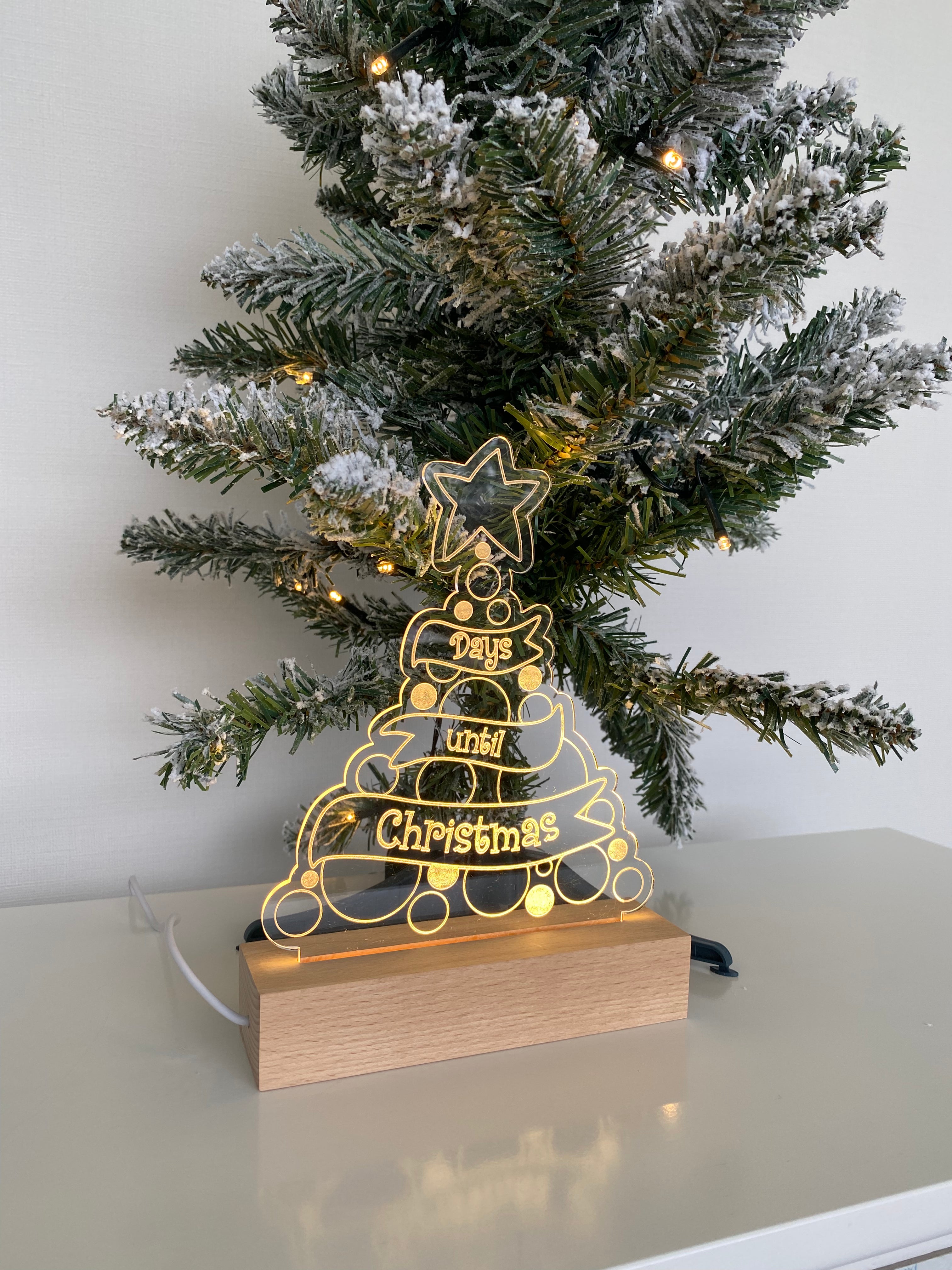 Christmas Countdown Night Light placed next to a mini Xmas tree, made from clear acrylic on a wooden base, complete with a whiteboard marker to write down each day of advent. Powered by USB.