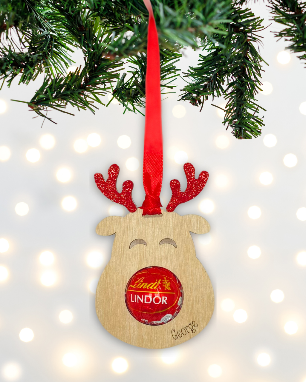 Laser-cut wooden Sweet-Nose Reindeer Ornament in red with a Lindt chocolate nose, engraved with the word George.