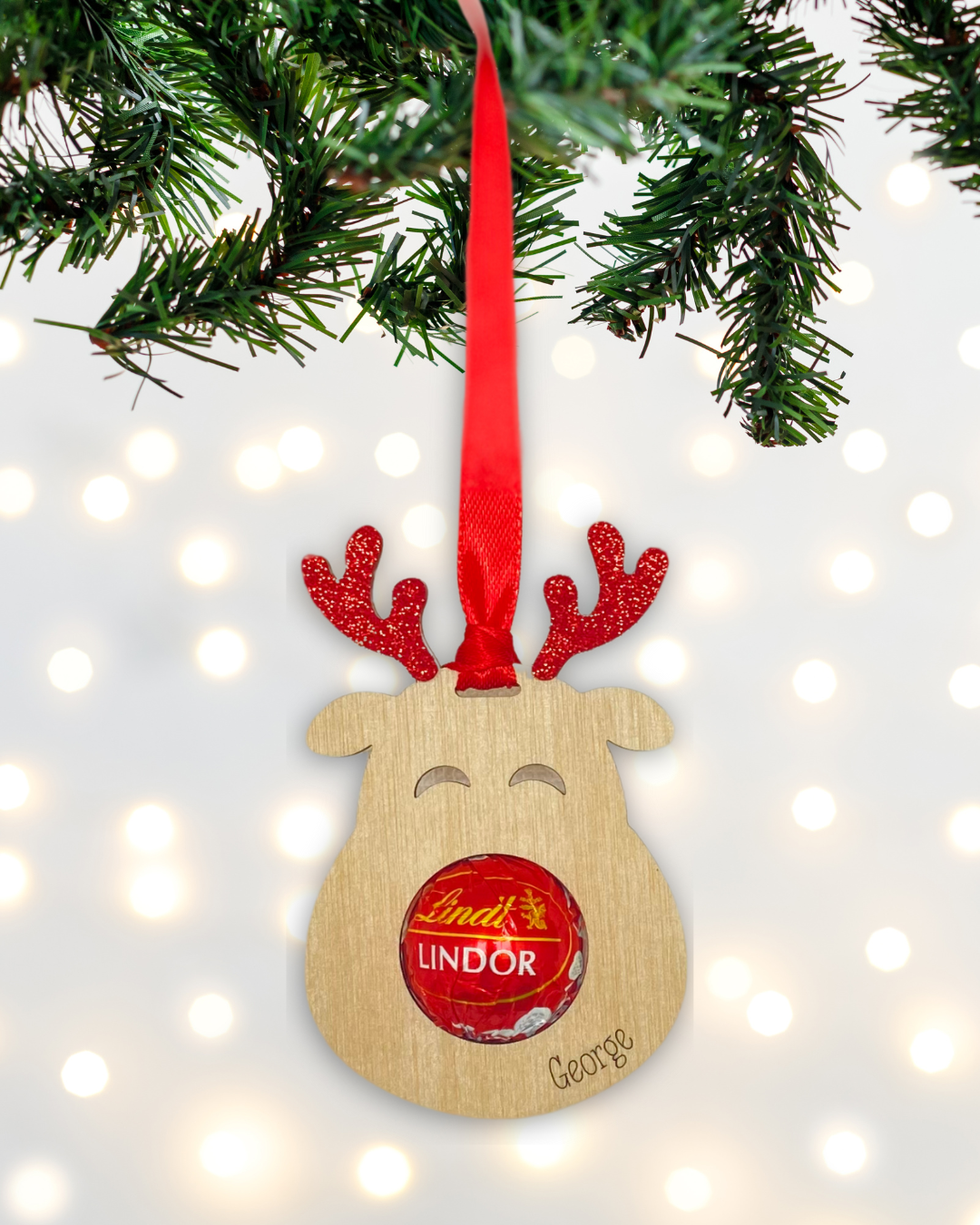 Laser-cut wooden Sweet-Nose Reindeer Ornament in red with a Lindt chocolate nose, engraved with the word George.