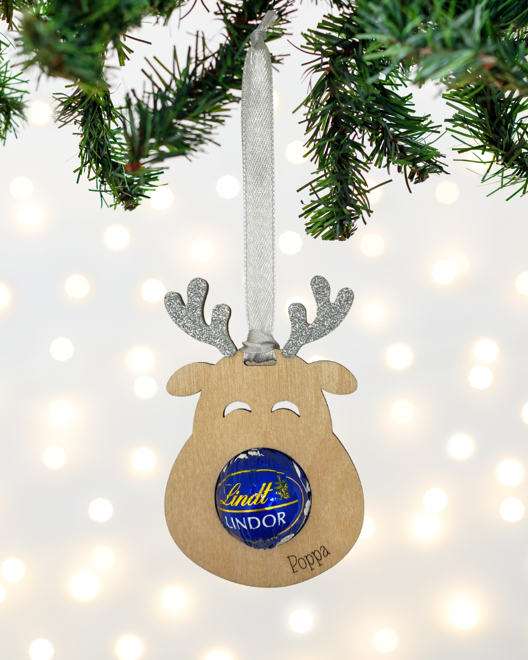 Laser-cut wooden Sweet-Nose Reindeer Ornament in silver with a Lindt chocolate nose, engraved with the word Poppa.